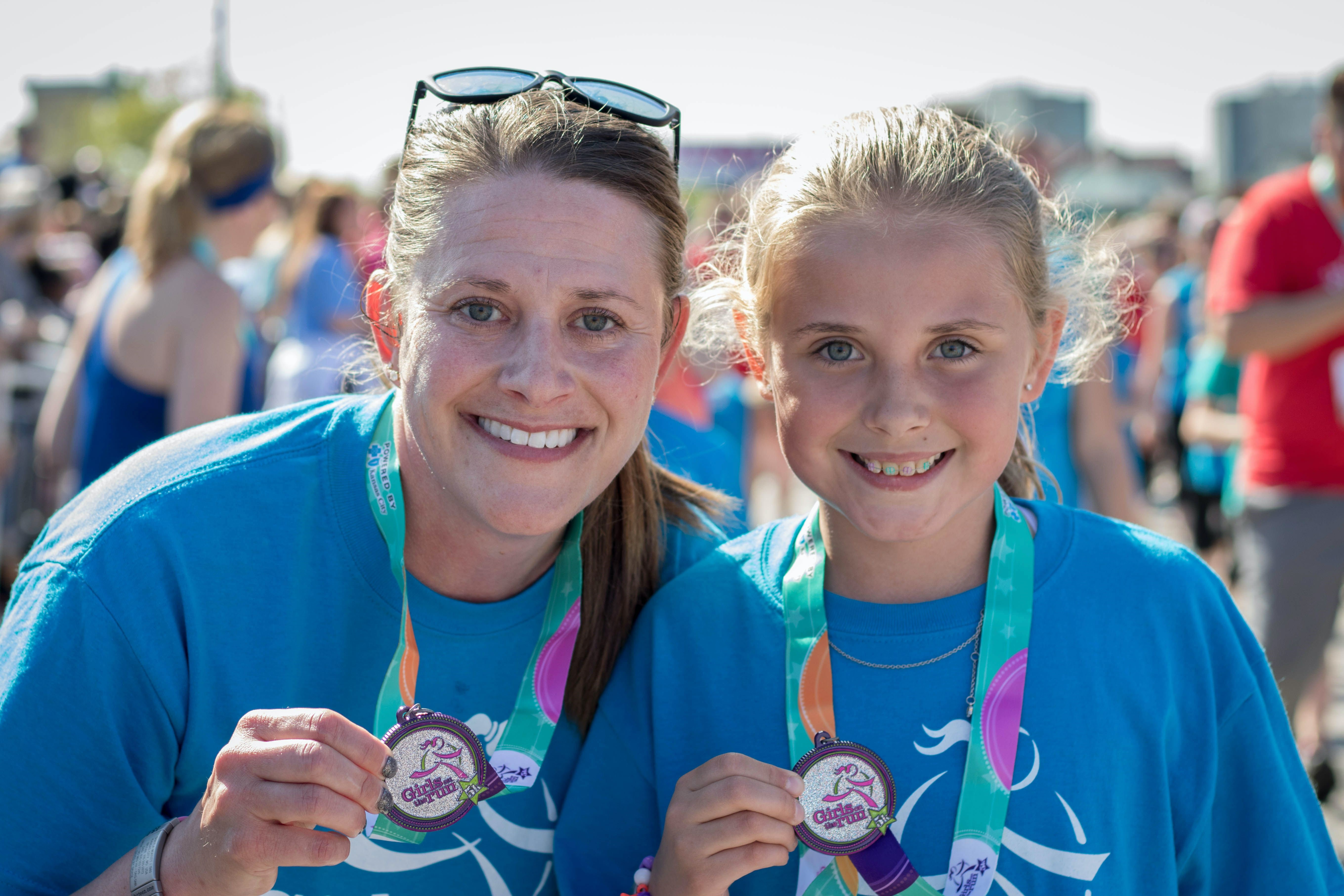 A Girls on the Run coach smiles while holding a program medal at the 5K